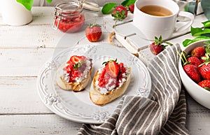 Homemade bruschetta with cottage cheese and strawberries for breakfast at white wooden background