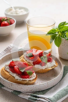 Homemade bruschettas with strawberries, cream cheese and basil in white plate on light background. Summer appetizer.