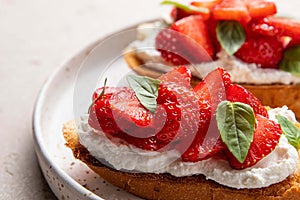 Homemade bruschettas with strawberries, cream cheese and basil in white plate on light background. Summer appetizer.