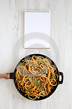 Homemade Bucatini all Amatriciana Pasta in a cast iron pan, blank notebook on a white wooden background, top view. Flat lay,