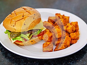 Homemade burger with cheese, lettuce, pickles and tomato slices on a white plate and fried sweet potatoes cubes , Selective focus