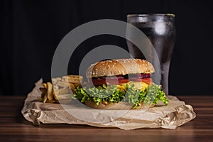 Homemade burger and french fries with oregano and frozen glass a tasty soda. Humburger served on pergament paper and wooden board.