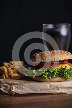 Homemade burger and french fries with oregano and frozen glass a tasty soda. Humburger served on pergament paper and wooden board. photo