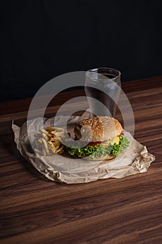 Homemade burger and french fries with oregano and frozen glass a tasty soda. Humburger served on pergament paper and wooden board.