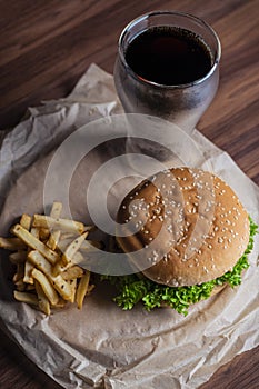 Homemade burger and french fries with oregano and frozen glass a tasty soda. Humburger served on pergament paper and wooden board.