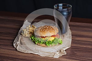 Homemade burger and french fries with oregano and frozen glass a tasty soda. Humburger served on pergament paper and wooden board.