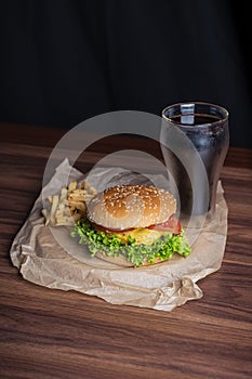 Homemade burger and french fries with oregano and frozen glass a tasty soda. Humburger served on pergament paper and wooden board.