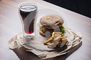 Homemade burger and french fries with oregano and frozen glass a tasty soda. Humburger served on pergament paper and wooden board.