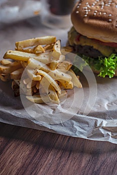 Homemade burger and french fries with oregano and frozen glass a tasty soda. Humburger served on pergament paper and wooden board.