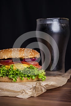 Homemade burger and french fries with oregano and frozen glass a tasty soda. Humburger served on pergament paper and wooden board. photo