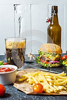 Homemade burgers with beef and fried potatoes and glass of cold dark beer on stone table