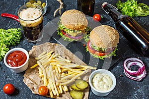 Homemade burgers with beef and fried potatoes and glass of cold dark beer on stone table