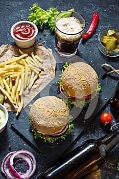 Homemade burgers with beef and fried potatoes and glass of cold dark beer on stone table