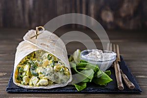 Homemade burrito wraps with boiled eggs, green wild garlic and sour cream for healthy breakfast on wooden board, closeup