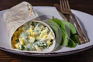 Homemade burrito wraps with boiled eggs, potato, green wild garlic and sour cream for healthy breakfast on plate, closeup