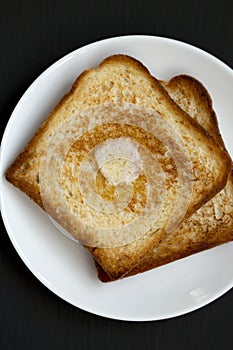 Homemade Buttered Toast on a white plate on a black background, top view. Flat lay, overhead, from above