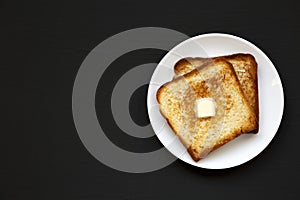 Homemade Buttered Toast on a white plate on a black background, top view. Flat lay, overhead, from above. Copy space