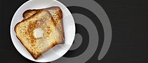 Homemade Buttered Toast on a white plate on a black background, top view. Flat lay, overhead, from above. Copy space