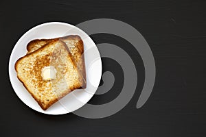 Homemade Buttered Toast on a white plate on a black background, top view. Flat lay, overhead, from above. Copy space