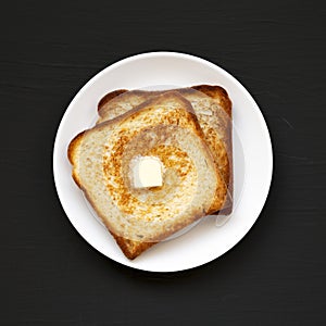 Homemade Buttered Toast on a white plate on a black surface, top view. Flat lay, overhead, from above