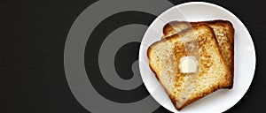 Homemade Buttered Toast on a white plate on a black surface, top view. Flat lay, overhead, from above. Copy space