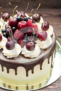 Homemade cake with melted chocolate decorated with whipped cream and fresh cheries on top. Rustic wooden background