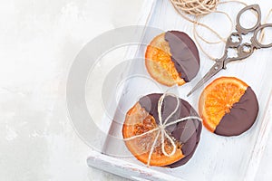 Homemade candied sliced oranges covered with chocolate on white tray, making sweet gifts, horizontal, copy space, top view