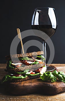 Homemade caprese sandwich and glass of red wine on board