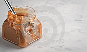 Homemade caramel sauce in a glass jar on a light table. Close-up, copy space. Sweet dessert