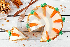 Homemade carrot cake with cream cheese frosting and slice being removed, above view table scene over white wood photo