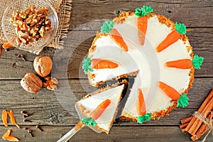 Homemade carrot cake with cream cheese frosting and slice being removed, top view table scene over wood