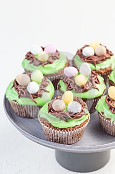 Homemade carrot cupcakes with cream cheese frosting and Easter chocolate eggs, on gray cake stand, vertical, copy space