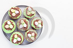 Homemade carrot cupcakes with cream cheese frosting and Easter chocolate eggs, on gray plate, horizontal, copy space, top view