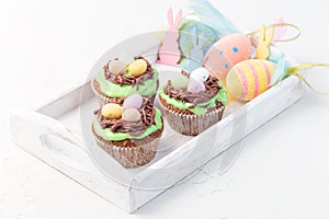 Homemade carrot cupcakes with cream cheese frosting and Easter decoration, on white wooden tray, horizontal