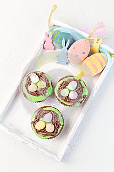 Homemade carrot cupcakes with cream cheese frosting and Easter decoration, on white wooden tray, vertical, top view