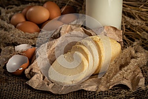 homemade cheese on craft paper next to milk and chicken eggs.