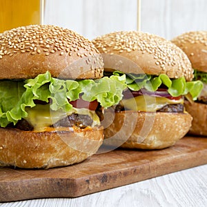 Homemade cheeseburgers and glass of beer on wooden board, side view. Close-up