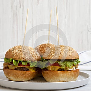 Homemade cheeseburgers on grey plate on white wooden surface, side view. Close-up