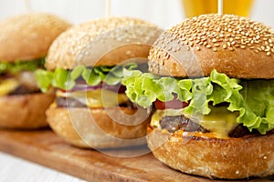 Homemade cheeseburgers on rustic wooden board and glass of cold beer, side view. Close-up