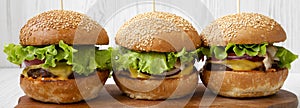 Homemade cheeseburgers on rustic wooden board over white wooden surface, side view. Closeup