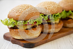 Homemade cheeseburgers on rustic wooden board, side view. Close-up. Selective focus