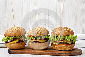 Homemade cheeseburgers on rustic wooden board on a white wooden surface, side view. Close-up