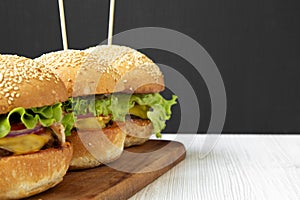 Homemade cheeseburgers on wooden board, side view. Copy space.