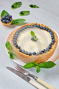 Homemade cheesecake with fresh berries on the white plate decorated with blueberries, mint leaves, knife and fork