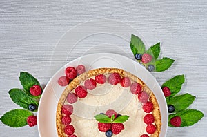 Homemade cheesecake with fresh berries on the white plate decorated with raspberries and blueberries, mint on the gray table