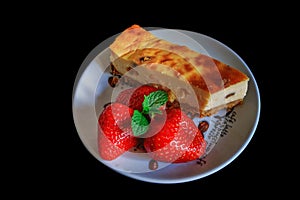 Homemade cheesecake on a plate decorated with fresh strawberries and mint leaves