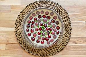 Homemade cheesecake is topped with fresh cherries and a sprig of mint in round cake pan on wooden table