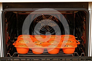 Homemade cherry cupcakes baked in a red silicone mold inside a home oven.