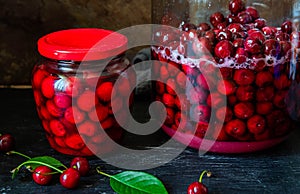 Homemade cherry preserves in a glass jar and fresh pitted red cherries preserved in sugar syrup. Canned organic food