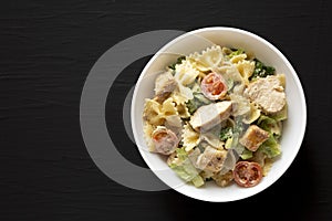 Homemade Chicken Caesar Pasta Salad in a white bowl on a black background, top view. Flat lay, overhead, from above. Space for
